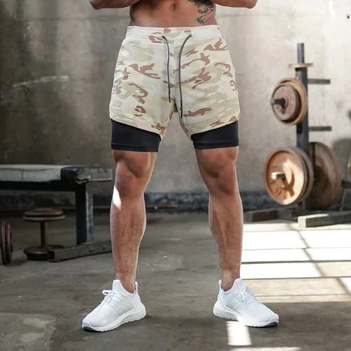 Pantaloncini sportivi mimetici da uomo in palestra, design a doppio strato, ideali per allenamento e fitness, con pesi sullo sfondo.