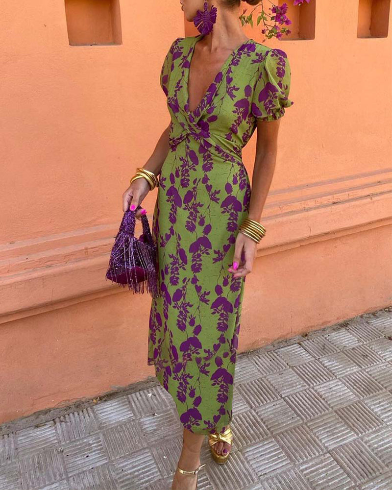 Abito lungo verde con stampa floreale viola, maniche a sbuffo, accessori coordinati, borsa frange viola, sandali dorati. Moda estiva elegante.