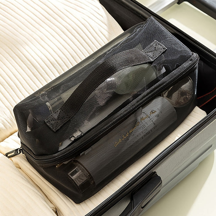 Borsa da viaggio trasparente nera con cerniera, contenente articoli da toeletta, posizionata su una valigia aperta. Accessori viaggio, organizzazione bagagli.