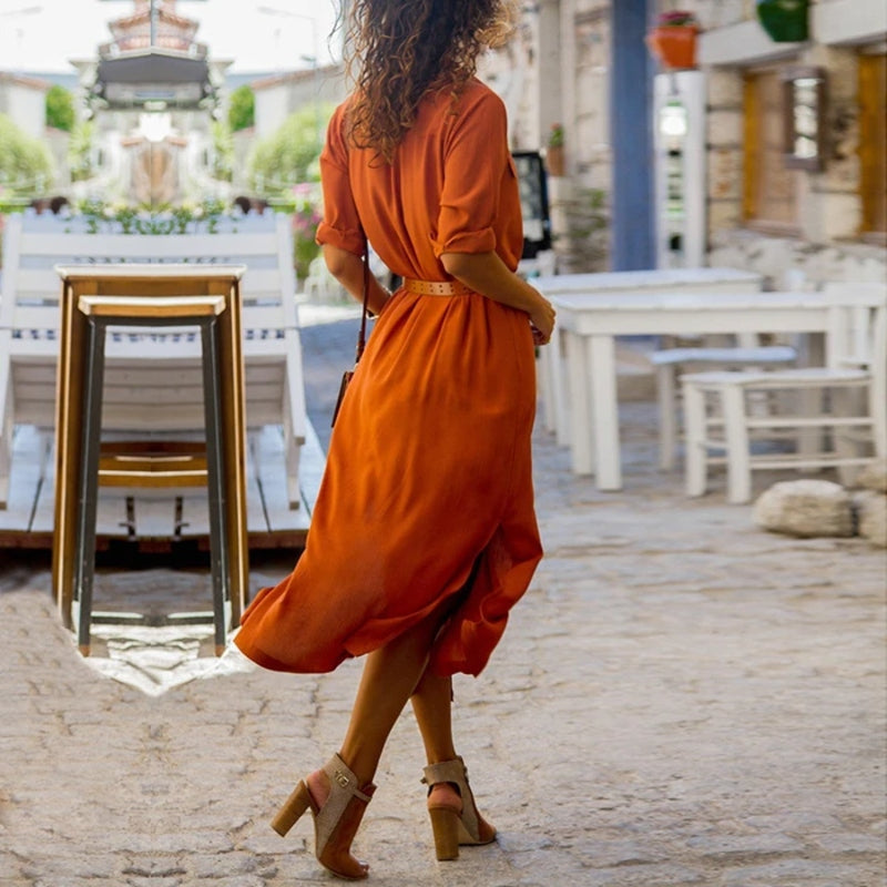 Donna con abito arancione cammina in strada acciottolata, indossando sandali con tacco. Moda estiva, abbigliamento casual elegante, stile urbano.