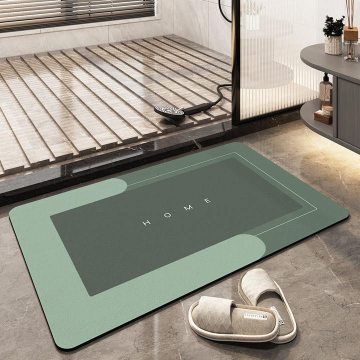 Tappeto da bagno verde con scritta "HOME", design moderno, antiscivolo, posizionato su pavimento in marmo, accanto a pantofole imbottite.