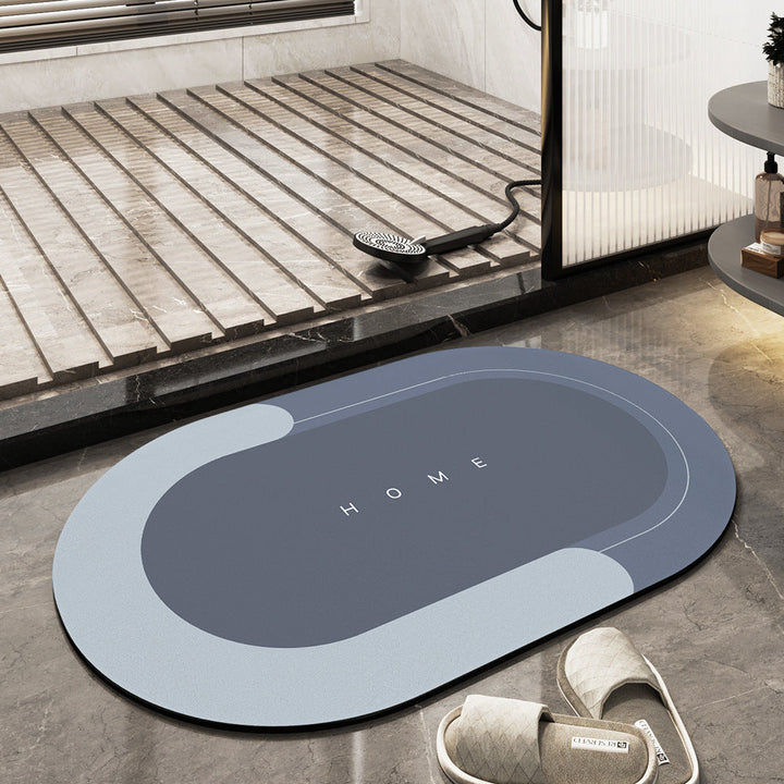 Tappeto da bagno ovale blu e grigio con scritta "HOME", posizionato su pavimento in marmo vicino a doccia moderna e pantofole beige.