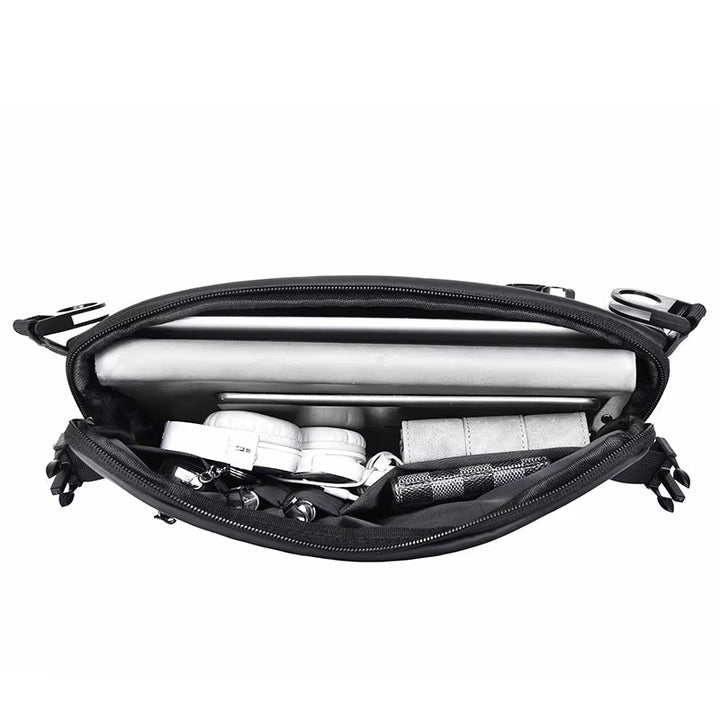 Borsa a tracolla nera aperta con laptop, cuffie, portafoglio e accessori. Design compatto, ideale per lavoro e viaggio. Tasche organizzate.