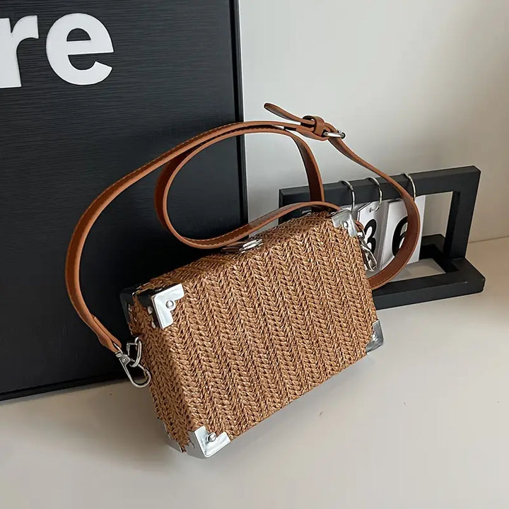 Borsa a tracolla in paglia intrecciata con angoli rinforzati in metallo e cinturino in pelle marrone, design elegante e moderno.