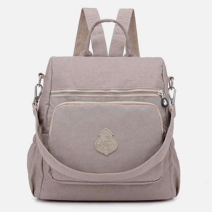 Zaino beige in tessuto impermeabile con tasca frontale con zip, spallacci regolabili e manico superiore. Design elegante e pratico per uso quotidiano.