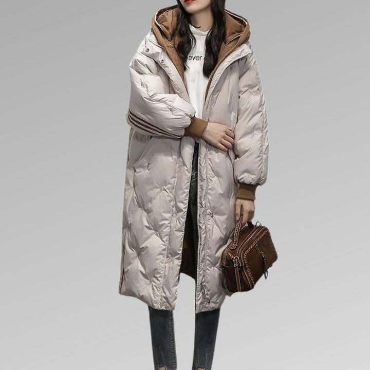 Giacca invernale lunga da donna, imbottita, colore bianco, con cappuccio marrone, abbinata a jeans e borsa marrone. Moda casual invernale.