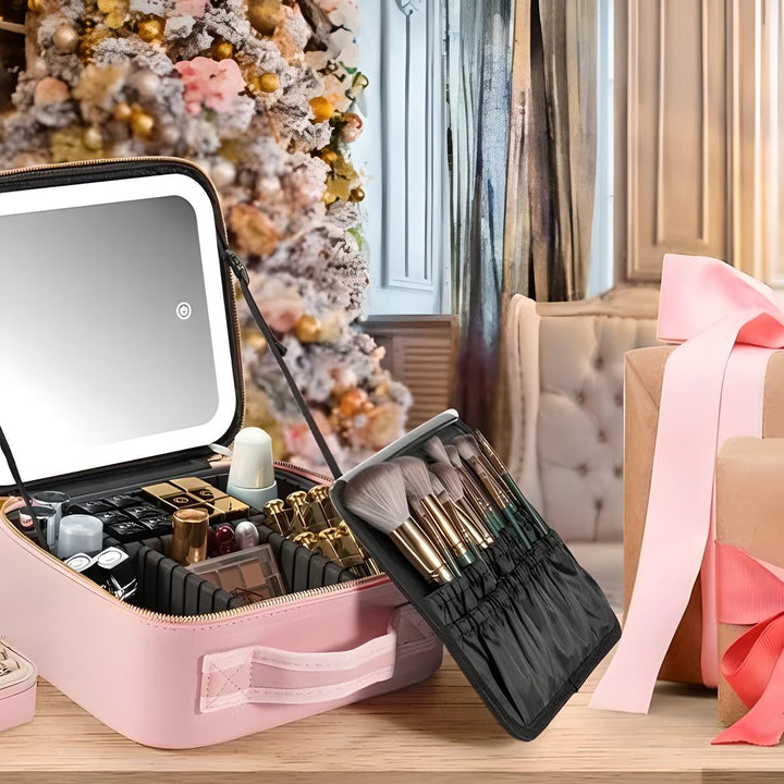 Astuccio trucco rosa con specchio LED, pennelli e cosmetici, davanti a un albero di Natale decorato e un regalo incartato con nastro rosa.