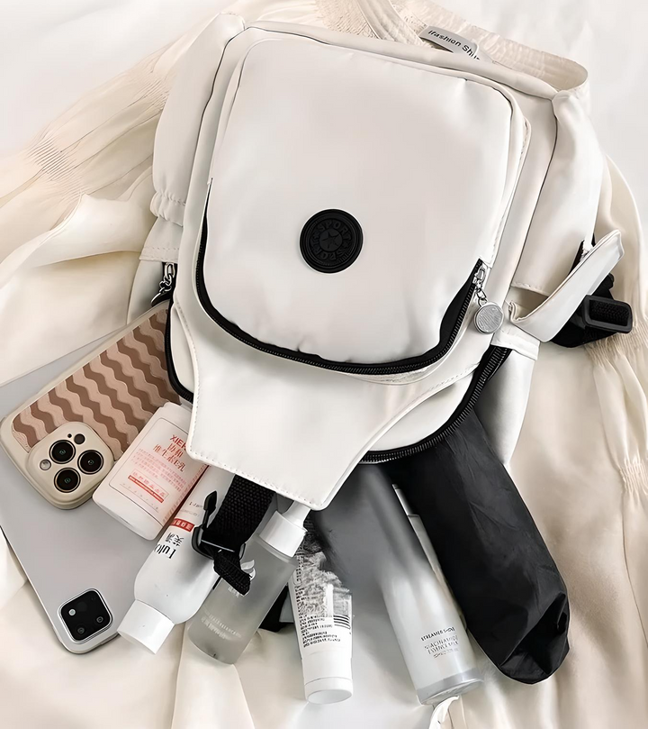 Zaino bianco elegante con tasche multiple, circondato da smartphone, cosmetici e ombrello nero. Accessori moda, tecnologia e bellezza.