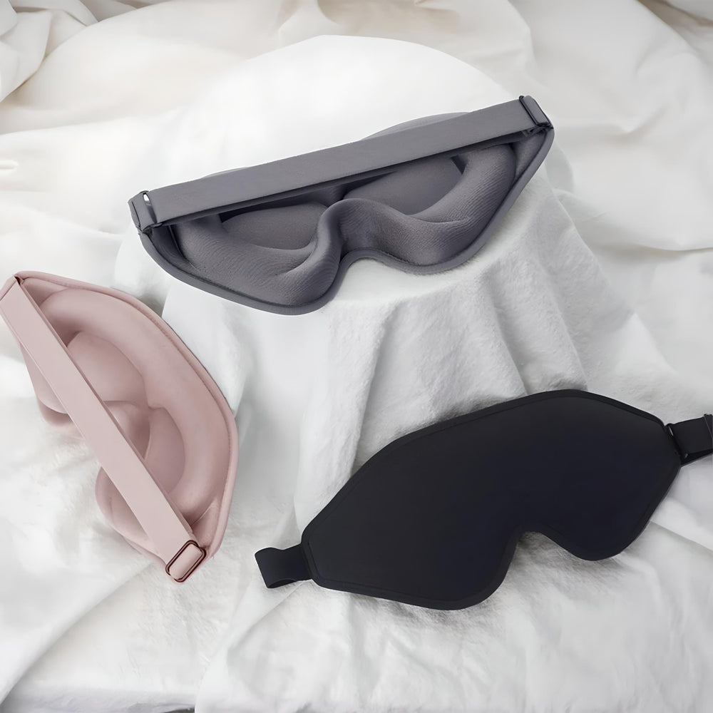 Tre maschere per dormire in tessuto morbido: grigio, rosa e nero, su sfondo bianco. Accessori per il sonno, comfort, relax.