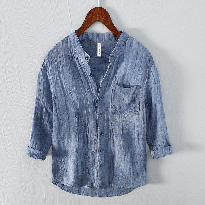 Camicia di lino blu da uomo, maniche lunghe, colletto alla coreana, tasca frontale, design casual, appesa su gruccia di legno.