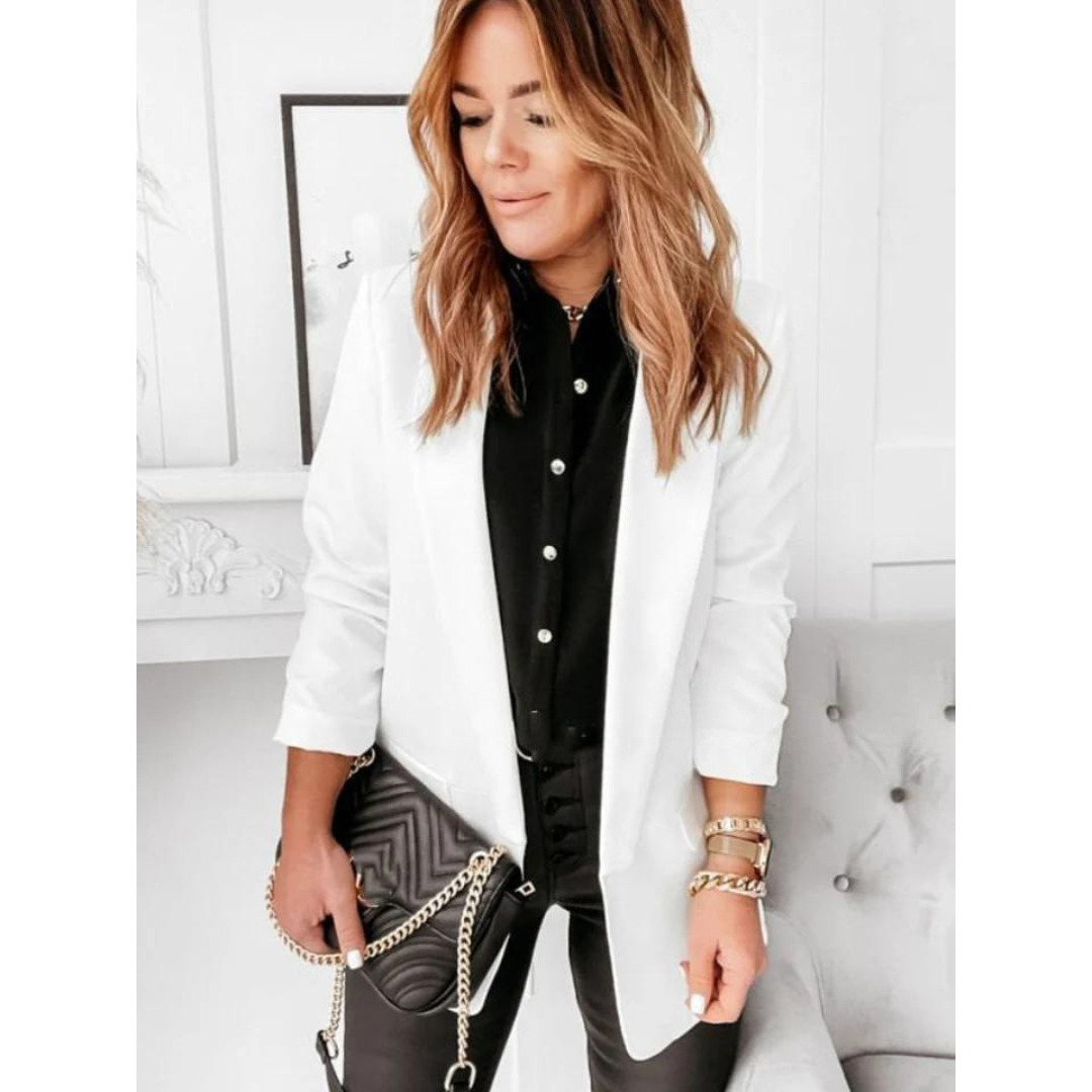 Donna con giacca bianca elegante, camicia nera e pantaloni in pelle. Tiene una borsa a tracolla nera con catena dorata. Stile moda contemporanea.