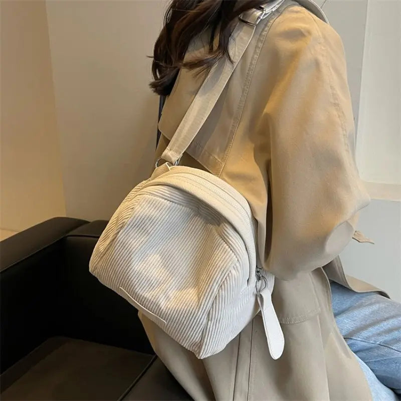 Zaino in velluto a coste bianco su donna con cappotto beige, moda autunno, accessorio casual elegante, ideale per shopping e viaggi urbani.