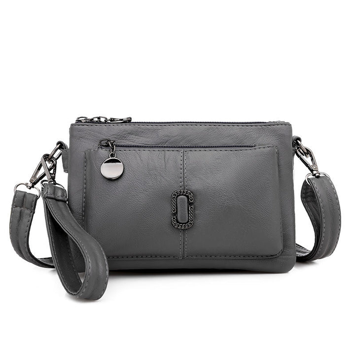 Borsa a tracolla in pelle grigia con tasca frontale, chiusura a zip e dettagli metallici. Elegante e pratica per uso quotidiano.