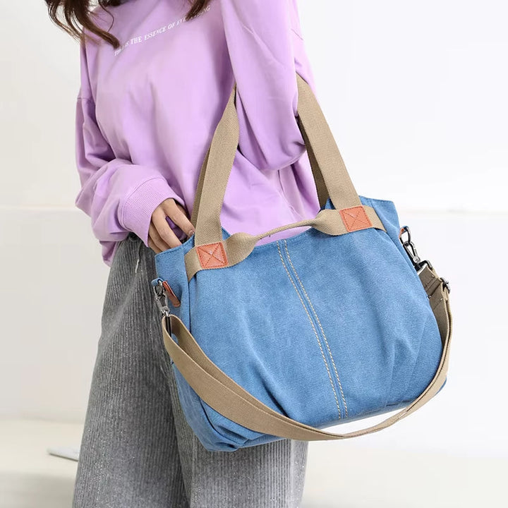 Borsa a tracolla in denim blu con manici beige, indossata da una persona con maglia viola. Design casual, ideale per moda quotidiana.