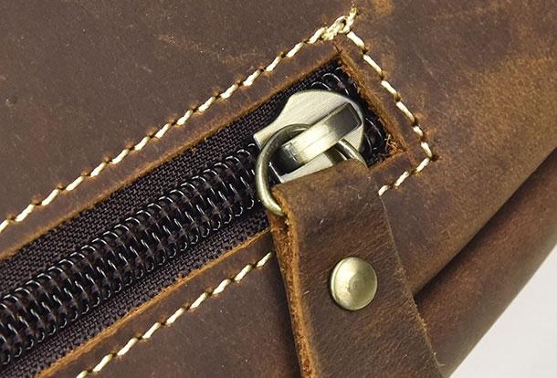 Cerniera in metallo su borsa in pelle marrone, cuciture bianche a contrasto, dettaglio artigianale, accessorio moda elegante e resistente.