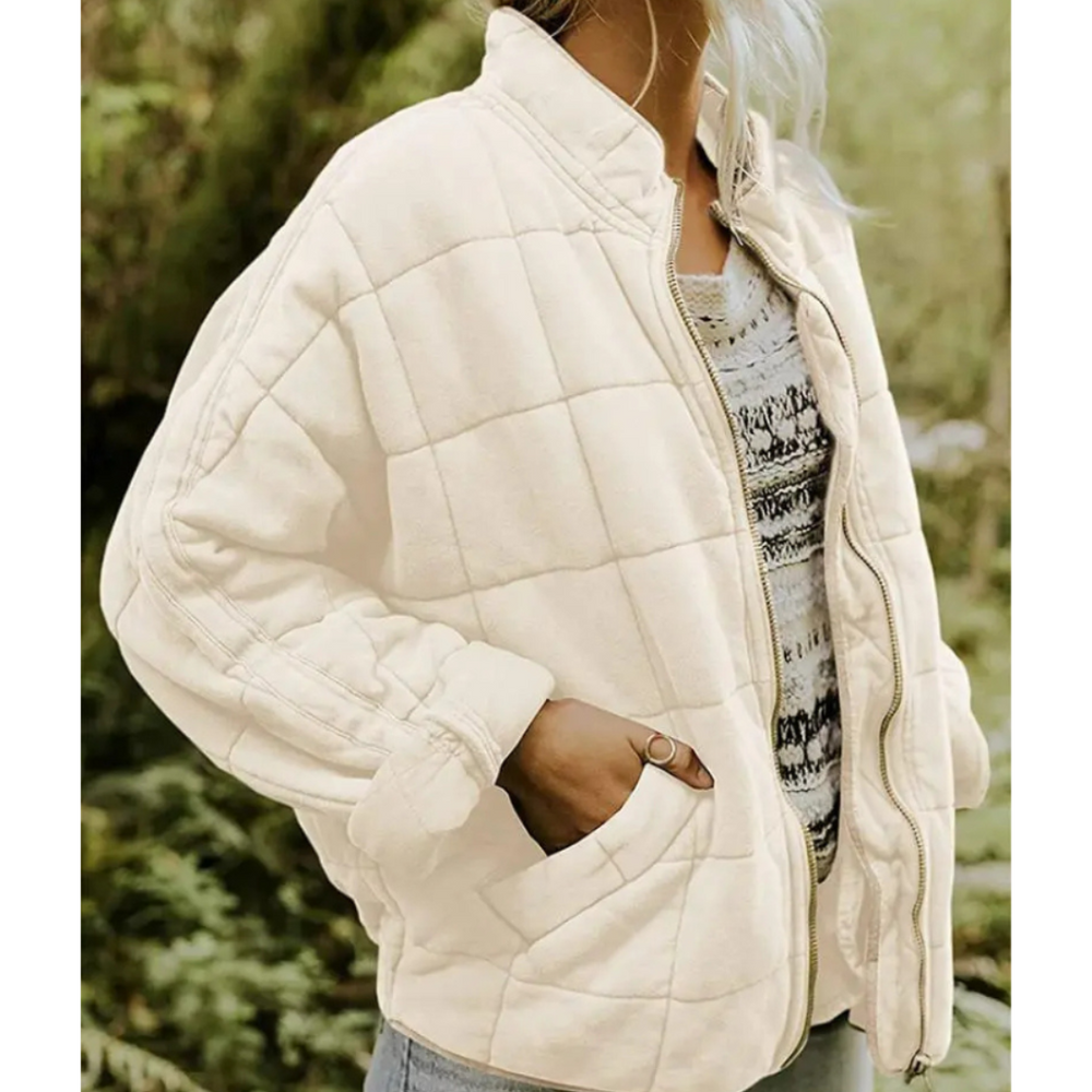 Giacca trapuntata beige da donna, stile casual, con zip frontale e tasche laterali, indossata su maglia a righe. Moda autunnale, abbigliamento femminile.
