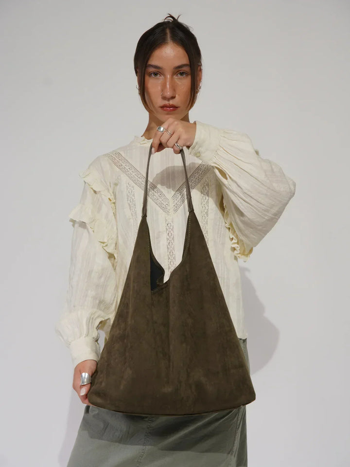 Donna con borsa a spalla in pelle scamosciata marrone, indossa camicia bianca con dettagli in pizzo. Moda donna, accessori eleganti, stile casual.