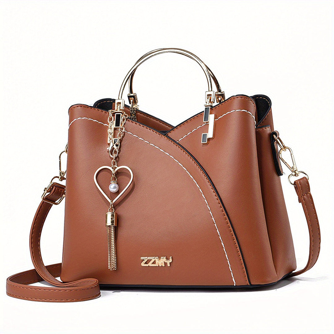Borsa a mano in pelle marrone con tracolla, decorata con ciondolo a cuore e dettagli metallici dorati. Elegante accessorio moda donna.