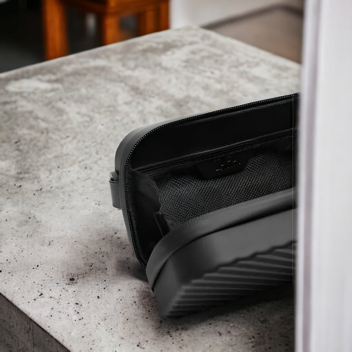 Borsa da toilette nera su tavolo in cemento, design moderno e minimalista, ideale per viaggi, accessori da bagno, organizer compatto ed elegante.