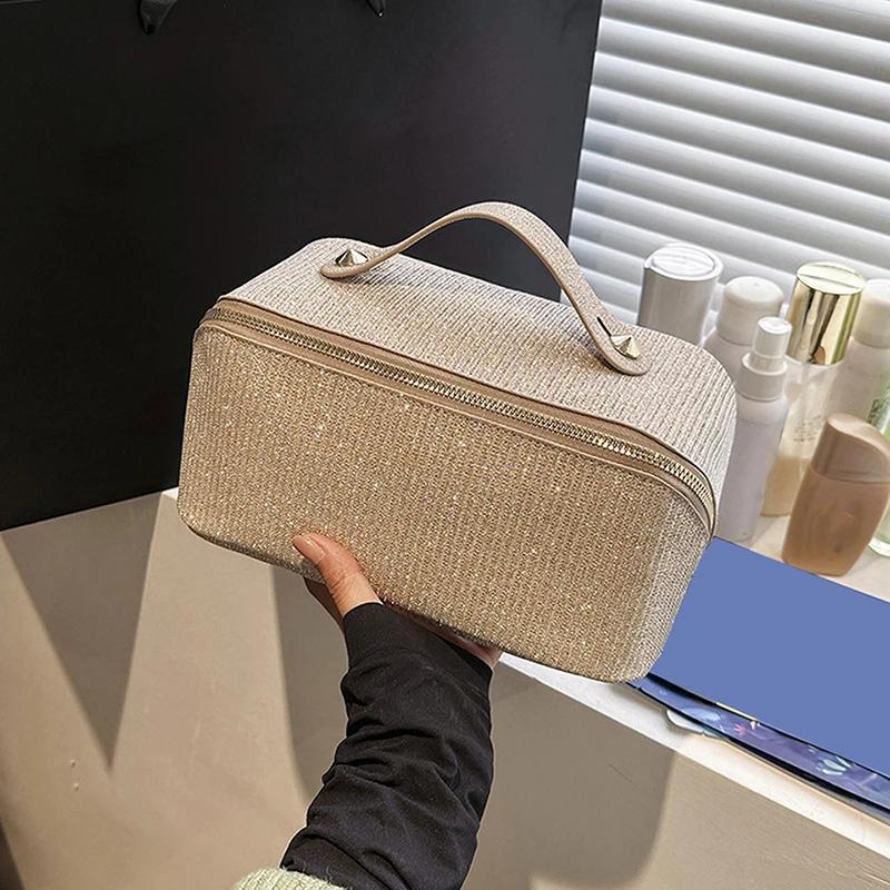 Borsa cosmetica beige con manico, tessuto glitterato, su sfondo di flaconi e finestra. Accessorio moda, organizer trucco elegante e pratico.