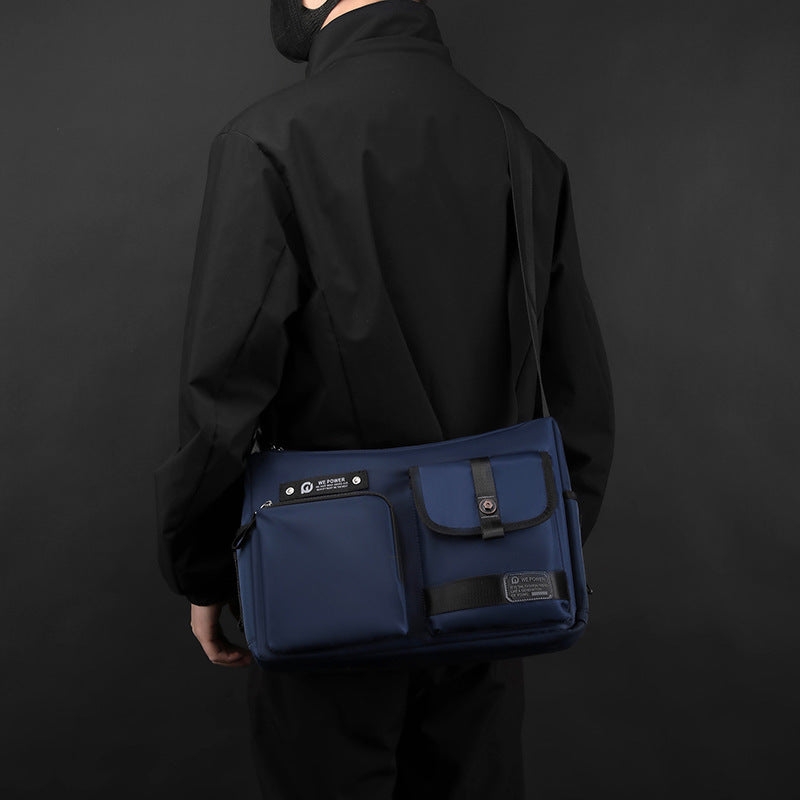 Borsa a tracolla blu scuro per laptop, design elegante e moderno, indossata da una persona in abbigliamento nero. Accessorio moda funzionale.