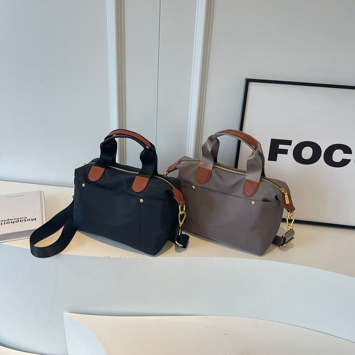 Due borse a mano eleganti in tessuto nero e grigio con dettagli in pelle marrone, esposte su un tavolo bianco. Design moderno e funzionale.