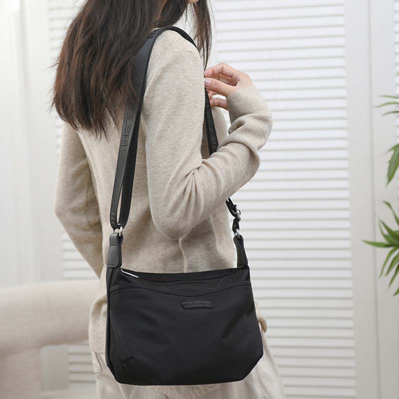 Borsa a tracolla nera in tessuto, indossata da una donna con maglione beige. Design elegante e pratico, ideale per uso quotidiano e lavoro.