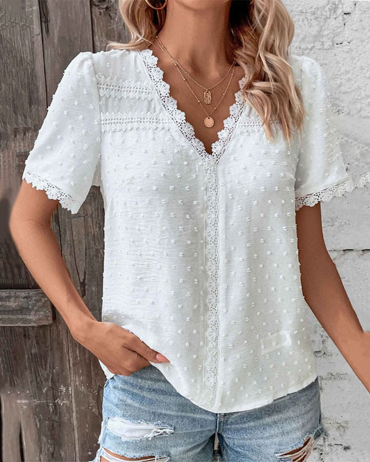 Blusa bianca in pizzo con maniche corte e scollo a V, abbinata a jeans strappati. Moda estiva donna, stile casual chic.