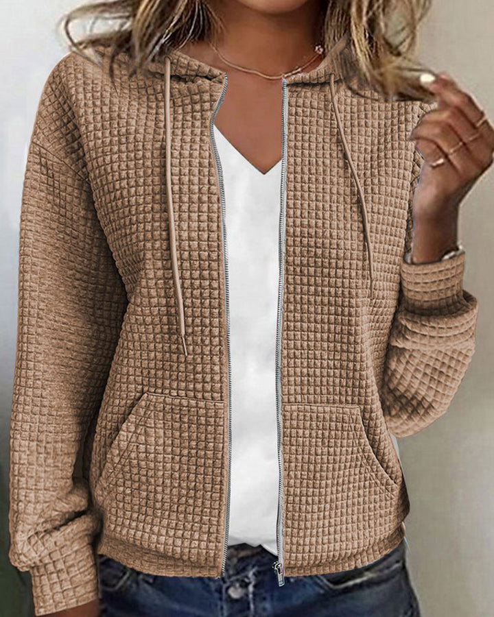 Giacca donna beige con cappuccio, tessuto trapuntato, chiusura zip, tasche frontali, abbinata a maglietta bianca. Moda casual autunnale.