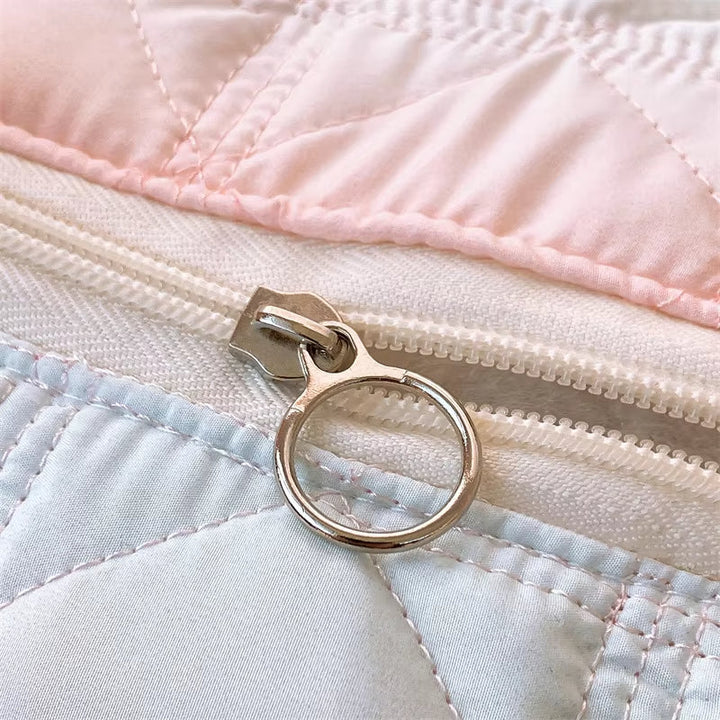 Cerniera in metallo su copripiumino trapuntato rosa e bianco, dettaglio tessuto morbido, chiusura resistente, accessorio camera da letto elegante.
