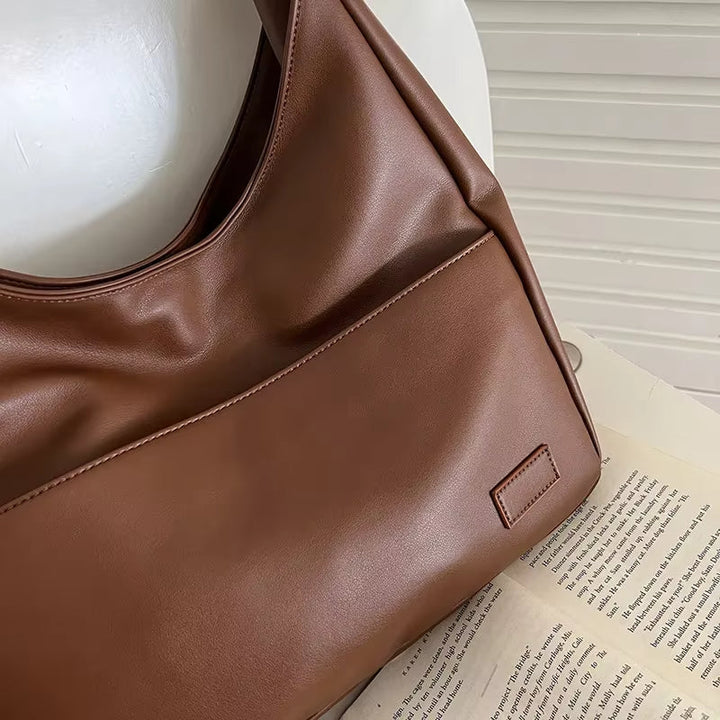 Borsa a spalla in pelle marrone su sedia bianca, design elegante e moderno, ideale per moda donna, accessorio versatile e di tendenza.