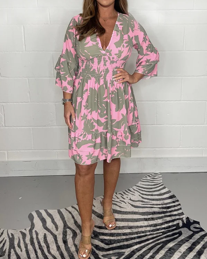 Abito donna floreale rosa e verde, maniche a tre quarti, scollo a V, indossato con sandali beige. Moda estiva elegante e casual.