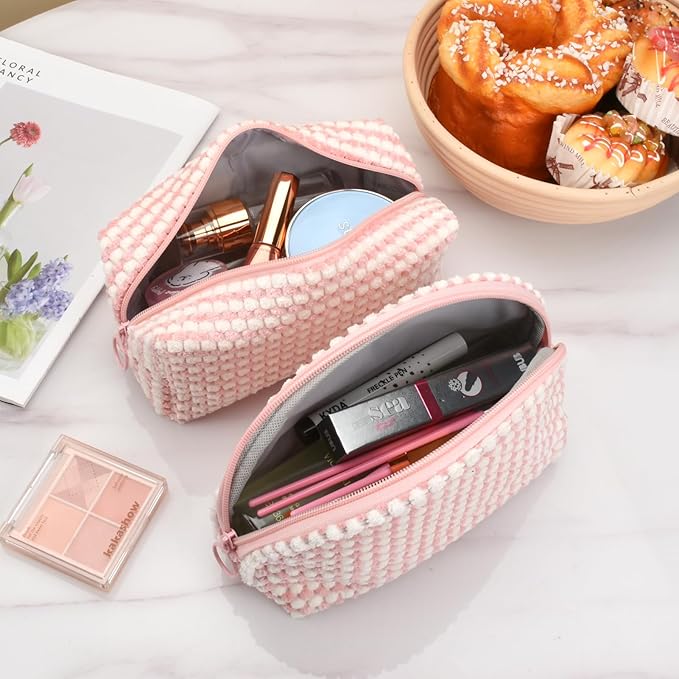 Due astucci cosmetici rosa a righe su tavolo di marmo, contenenti trucchi e accessori. Accanto, dolci e rivista. Accessori moda e bellezza.