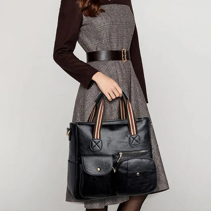 Donna con abito elegante e borsa a mano in pelle nera, tasche frontali, manici a righe. Accessorio moda femminile, stile classico e chic.