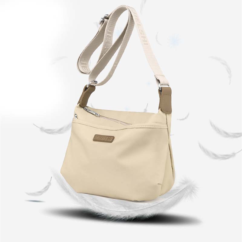 Borsa a tracolla beige in tessuto impermeabile, design elegante e minimalista, con cerniera e dettagli in pelle, ideale per uso quotidiano.