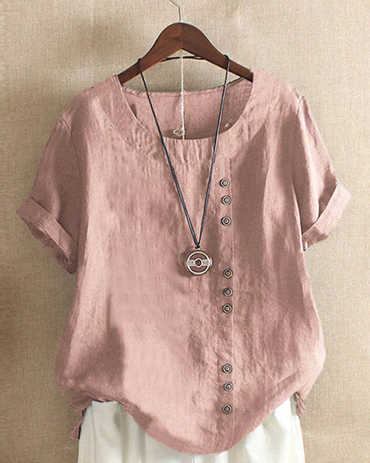 Blusa donna in lino rosa con bottoni decorativi, maniche corte risvolte, scollo rotondo, abbinata a collana pendente. Stile casual elegante.