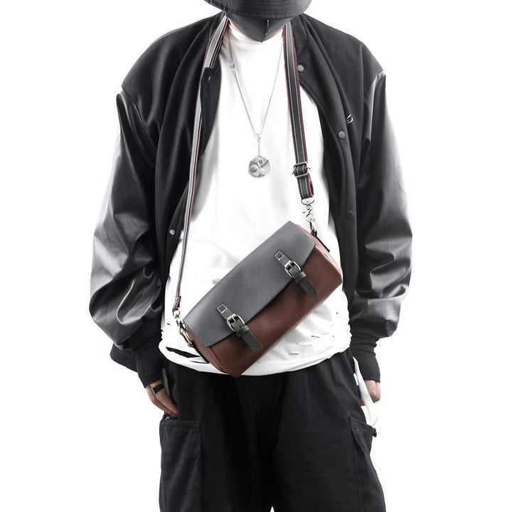 Uomo con giacca nera e borsa a tracolla in pelle bicolore, stile casual urbano. Accessorio moda maschile, tendenza streetwear.