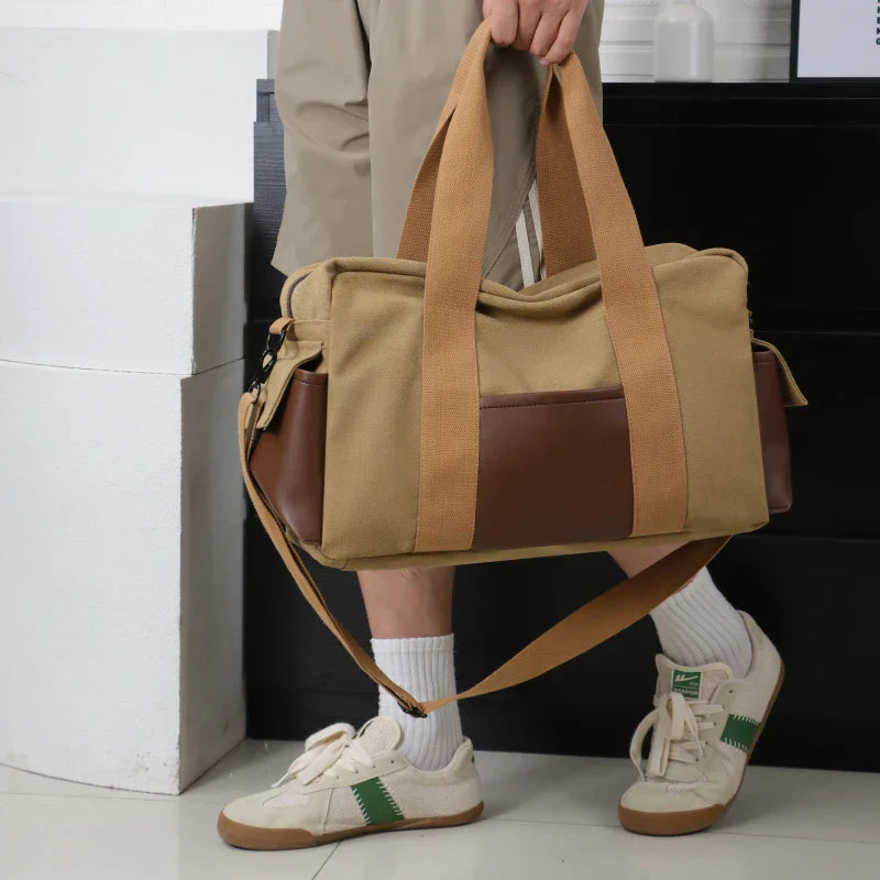 Borsa a tracolla in tela beige con dettagli in pelle marrone, manici robusti, indossata da una persona con pantaloni beige e scarpe sportive bianche.