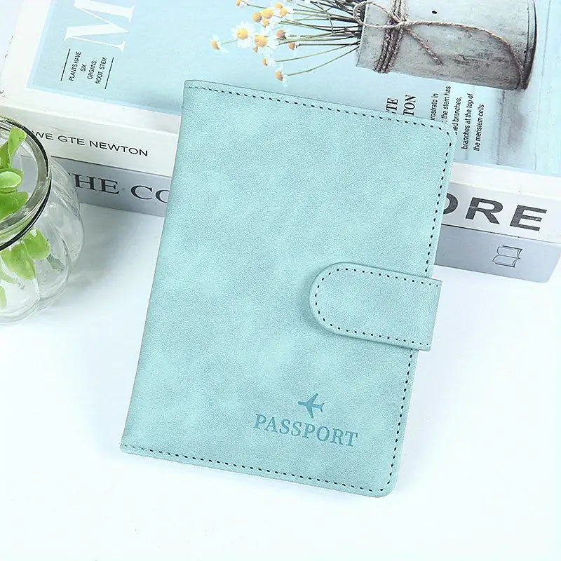 Custodia passaporto in pelle azzurra con chiusura a bottone, design elegante, ideale per viaggi, accessorio essenziale per protezione documenti.