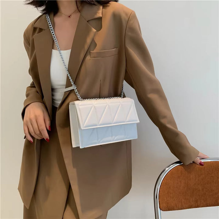 Donna con blazer marrone e borsa a tracolla bianca trapuntata, elegante e moderna, su sfondo neutro. Accessorio moda femminile di tendenza.