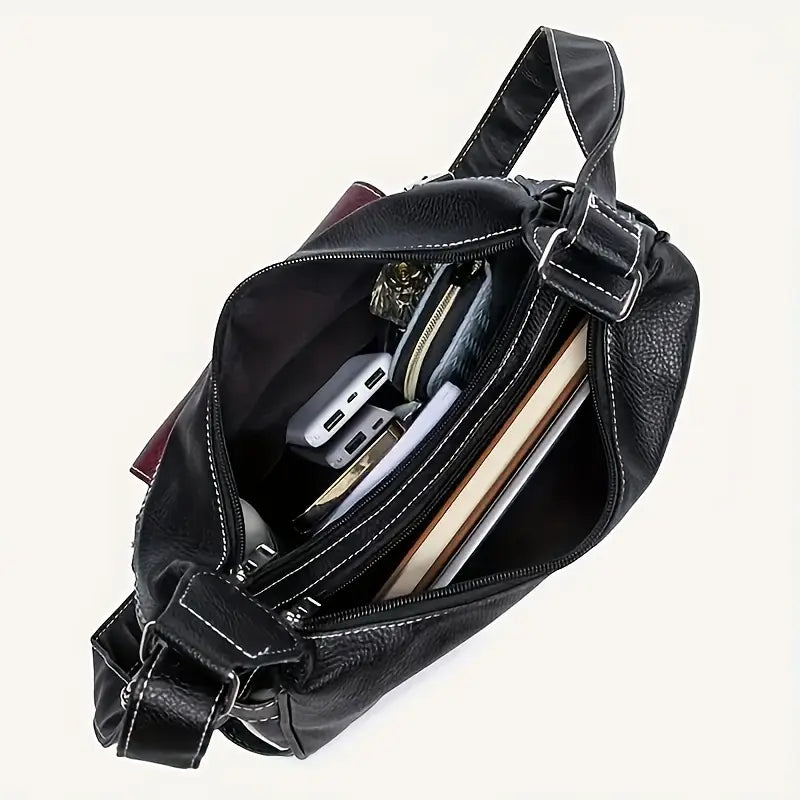 Borsa a tracolla in pelle nera aperta, con tasche interne, contenente portafoglio, power bank, libri e accessori. Elegante e spaziosa.