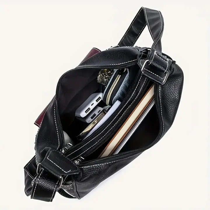 Borsa a tracolla in pelle nera aperta, con tasche interne, contenente portafoglio, power bank, libri e accessori. Elegante e spaziosa.