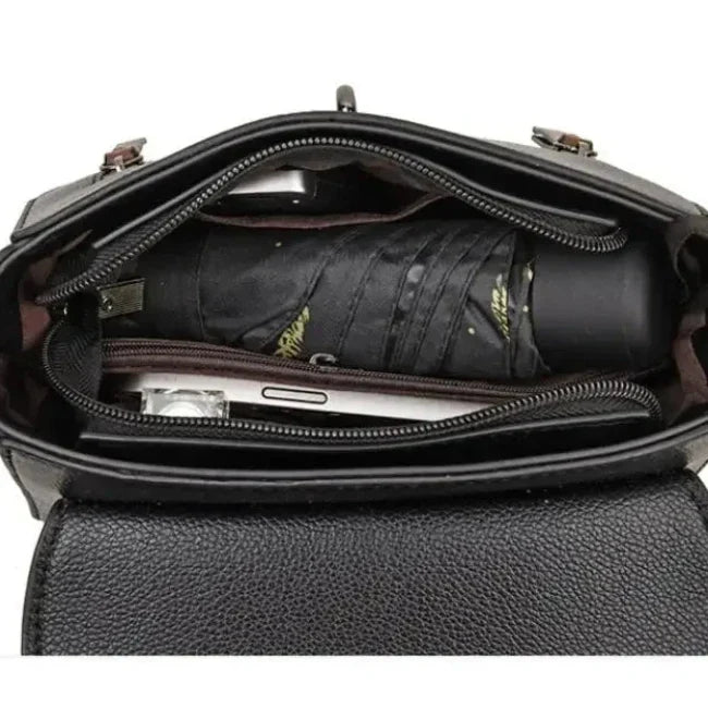 Interno di una borsa in pelle nera con ombrello pieghevole e smartphone. Accessori moda, borsa donna elegante, organizzazione pratica.