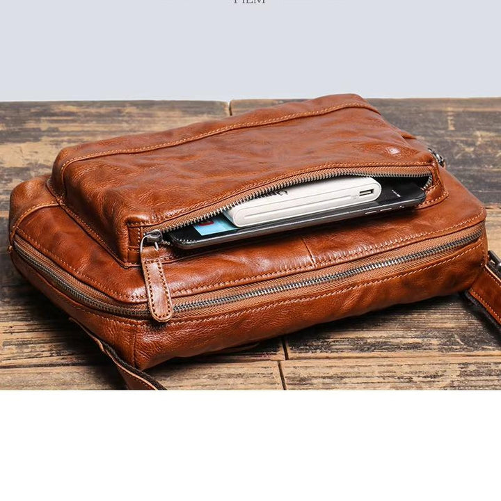 Borsa a tracolla in pelle marrone con cerniera aperta, mostra smartphone e portafoglio all'interno. Design elegante, ideale per uomo e donna.