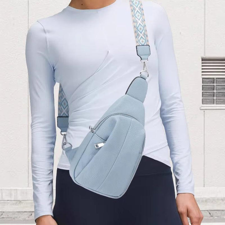Maglietta bianca a maniche lunghe con marsupio azzurro, tracolla decorata, indossato da persona su sfondo bianco. Accessorio moda casual.