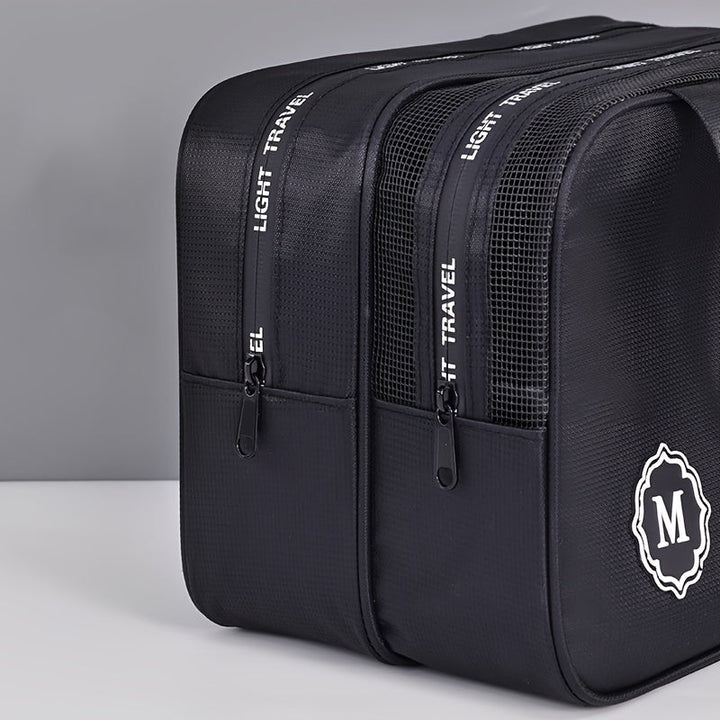 Zaino da viaggio nero con doppia cerniera, logo "M" e scritta "Light Travel". Design moderno, ideale per viaggi e uso quotidiano.