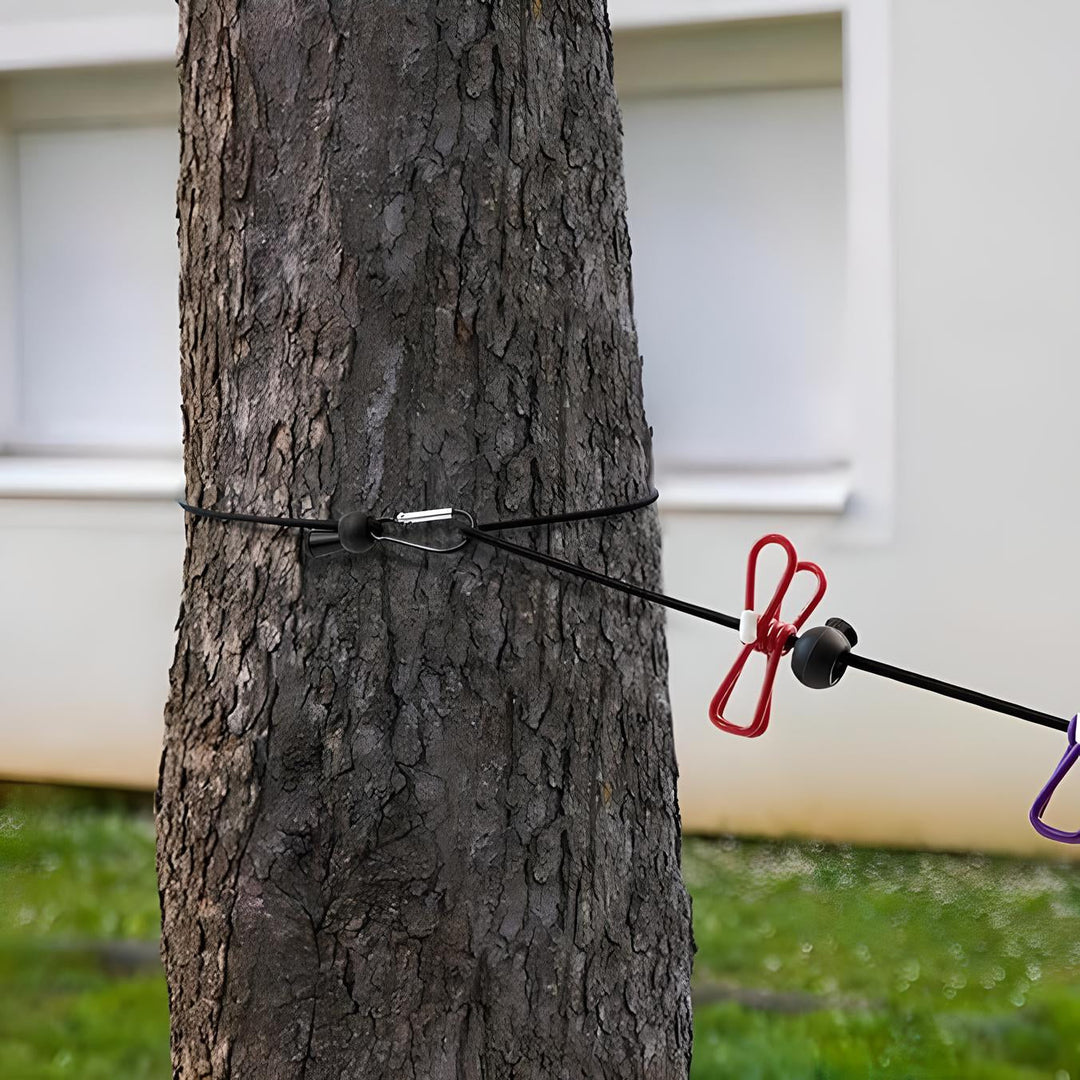 Corda elastica nera con ganci rossi e viola fissata a un albero, ideale per campeggio e attività all'aperto. Resistente e versatile.