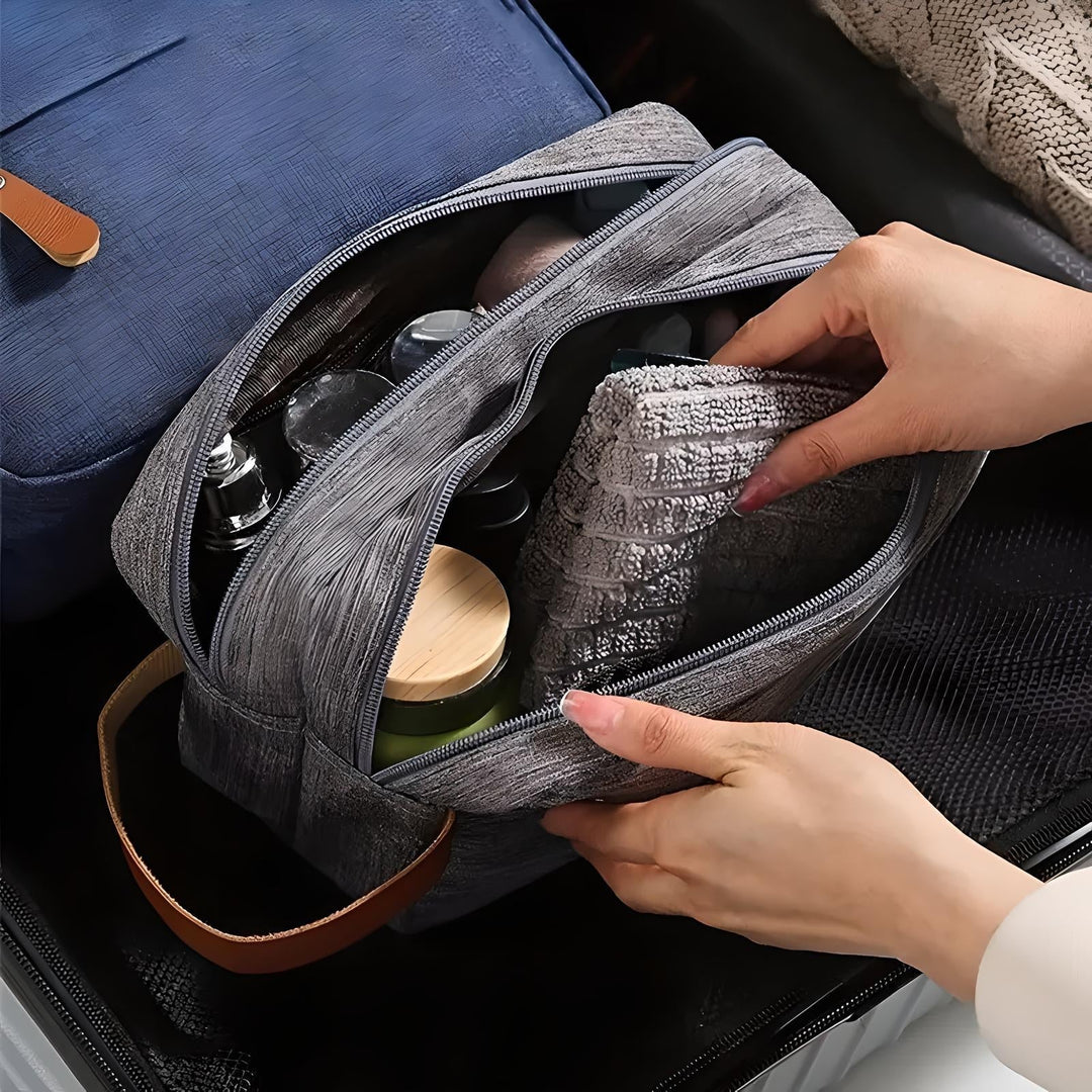 Borsa da toilette grigia aperta con prodotti cosmetici e asciugamano, mani femminili che organizzano, ideale per viaggi, accessori da bagno, valigia.