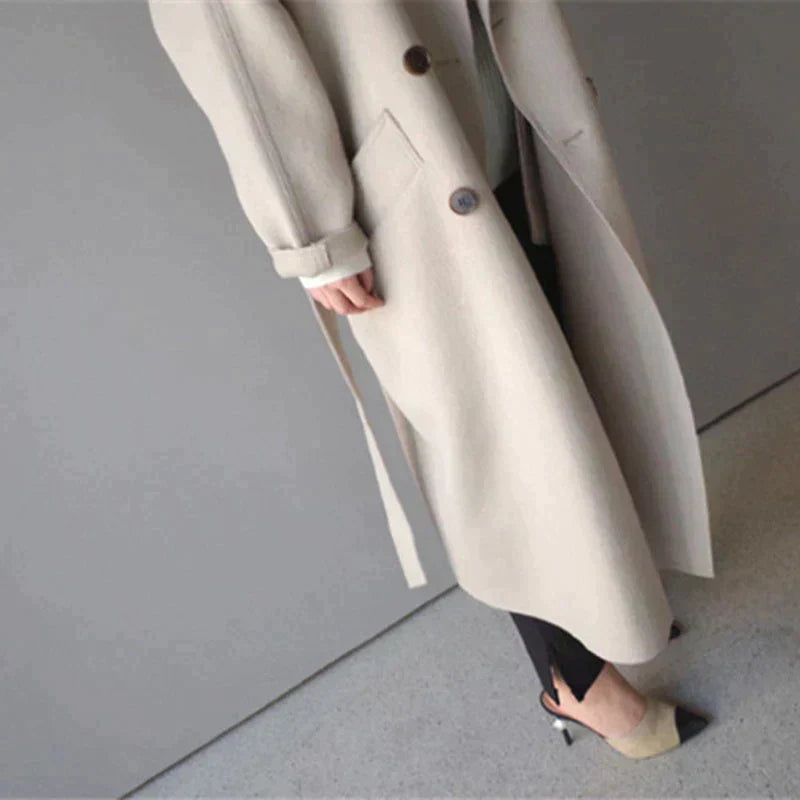 Cappotto beige elegante da donna, lungo, con bottoni e cintura, abbinato a pantaloni neri e tacchi. Moda autunnale, stile sofisticato.
