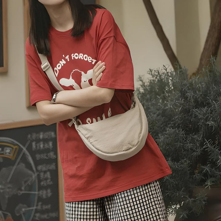 Donna con maglietta rossa grafica e borsa a tracolla beige, pantaloni a quadri. Moda casual, abbigliamento urbano, stile giovanile.